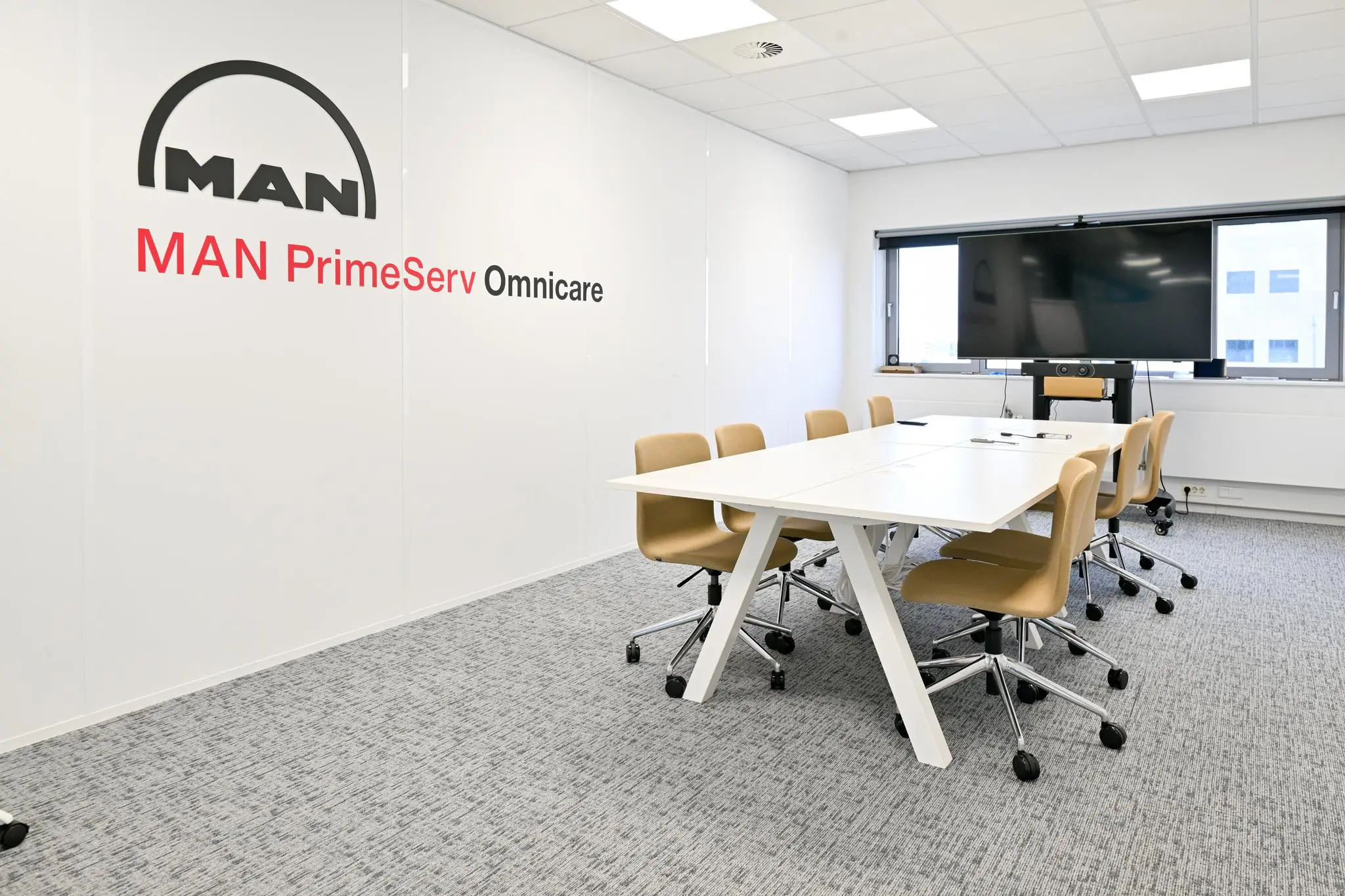 Moderne vergaderruimte bij MAN PrimeServ Omnicare in Rivium Quadrant met witte tafel, beige stoelen en groot beeldscherm.